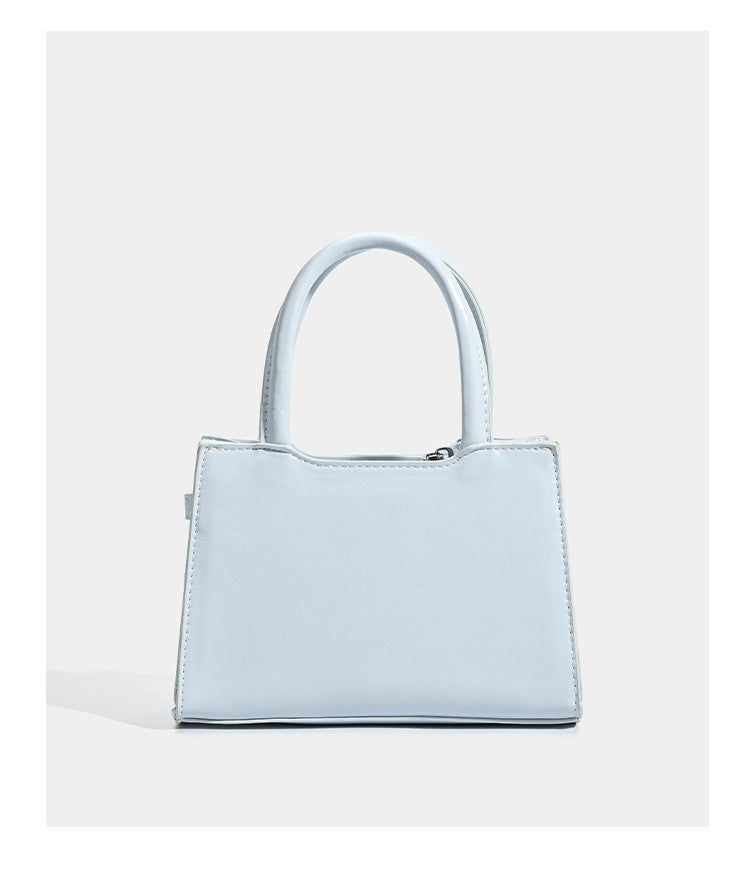 Small structured trapezoid mini top-handle bag with front belt-knot buckle detail and glossy leather-look finish, detail view