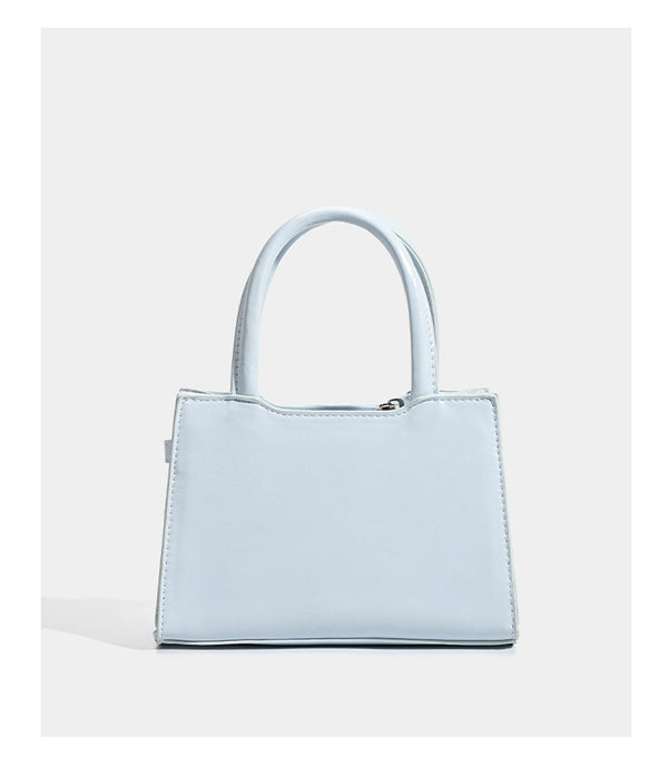 Small structured trapezoid mini top-handle bag with front belt-knot buckle detail and glossy leather-look finish, detail view