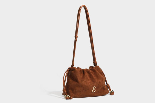 Suede-look drawstring shoulder bag in brown with smooth trim, knotted bead drawstring closure, slim adjustable strap, and