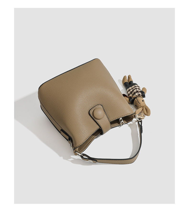 Structured taupe pebbled-texture bucket bag with top handle, silver ring hardware, tab-and-button closure, and knit bunny
