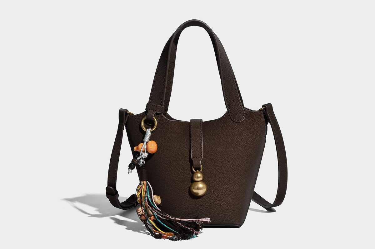 Kleine matte Beuteltasche mit genarbter Oberfläche, antikgoldfarbenen Ringbeschlägen, Perlen- und Quastenanhänger, kurzen Tragegriffen oben und