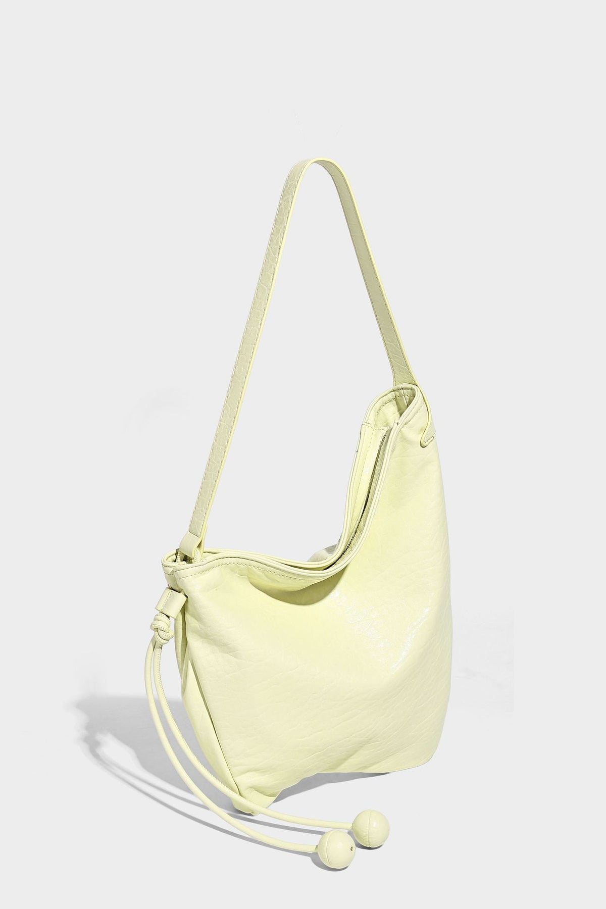Slouchy hobo shoulder bag in pale yellow with slim strap, drawstring bead closure, and pink tulip floral charm, detail view