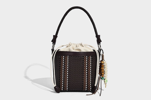 Small woven bucket bag with drawstring top, braided handle, detachable crossbody strap, and silver-tone ring hardware, detail