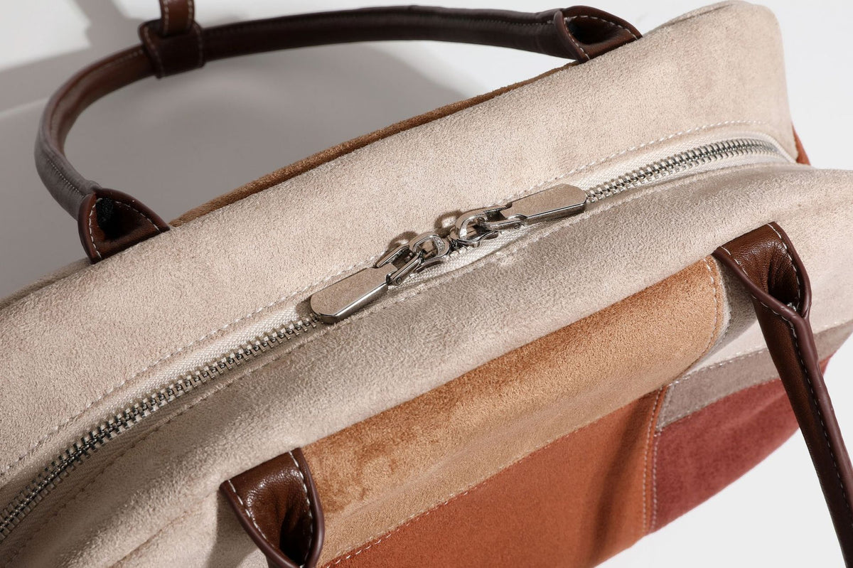 Boxy patchwork suede-look shoulder tote in tan, beige, rust, and brown panels with double brown straps and hanging doll