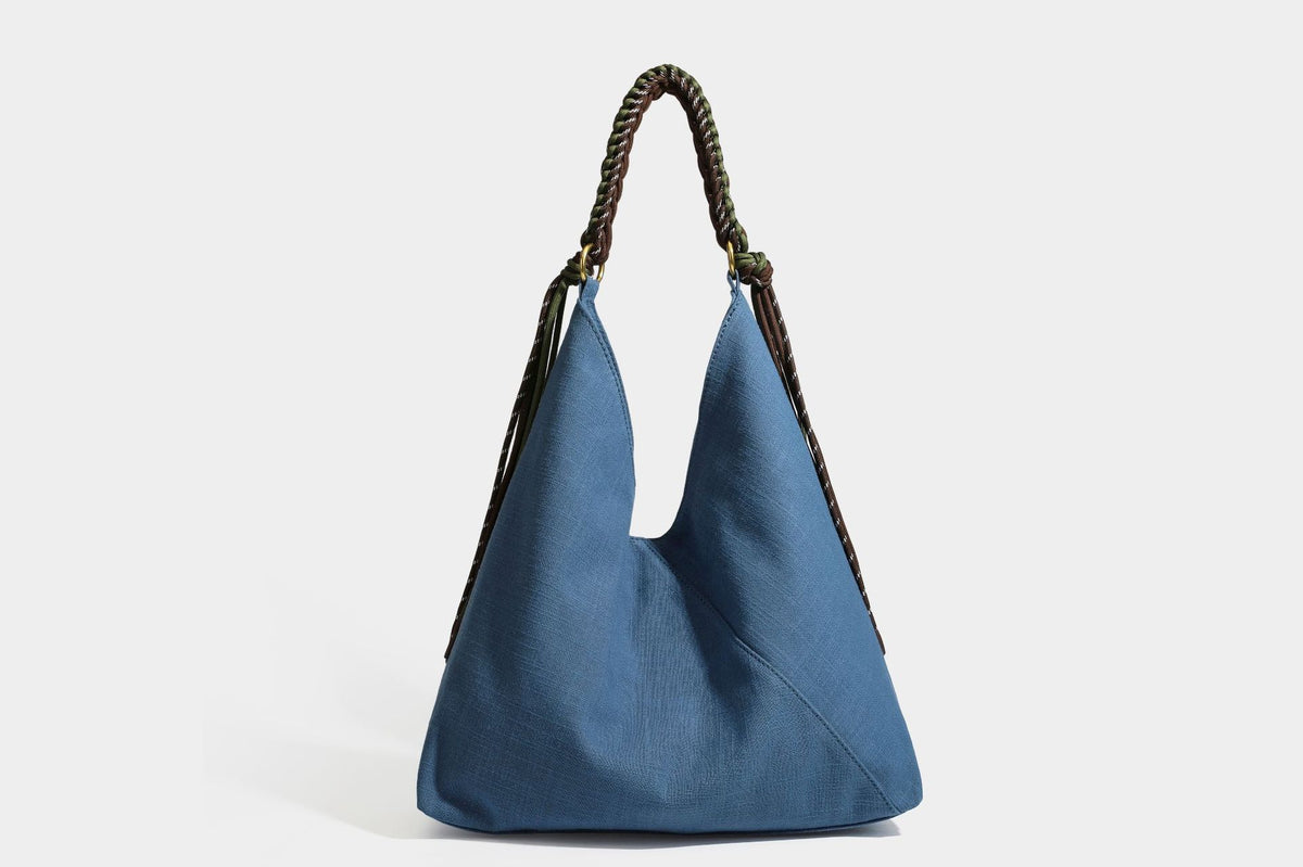 Soft slouchy cream canvas shoulder tote with braided brown and green cord handle, gold-tone ring hardware, and tassel trim