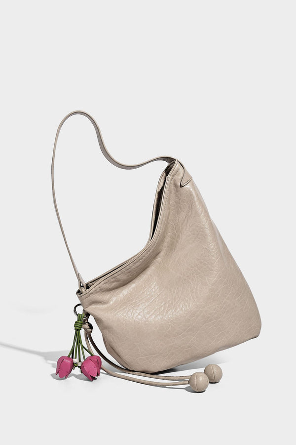 Slouchy hobo shoulder bag in pale yellow with slim strap, drawstring bead closure, and pink tulip floral charm, detail view