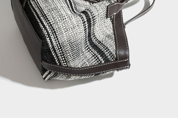 Schwarz-weiße gewebte Trapez-Tote-Bag mit dunklem Lederimitat-Besatz, weißen Kontrastnähten und zwei Henkeln, Detailansicht