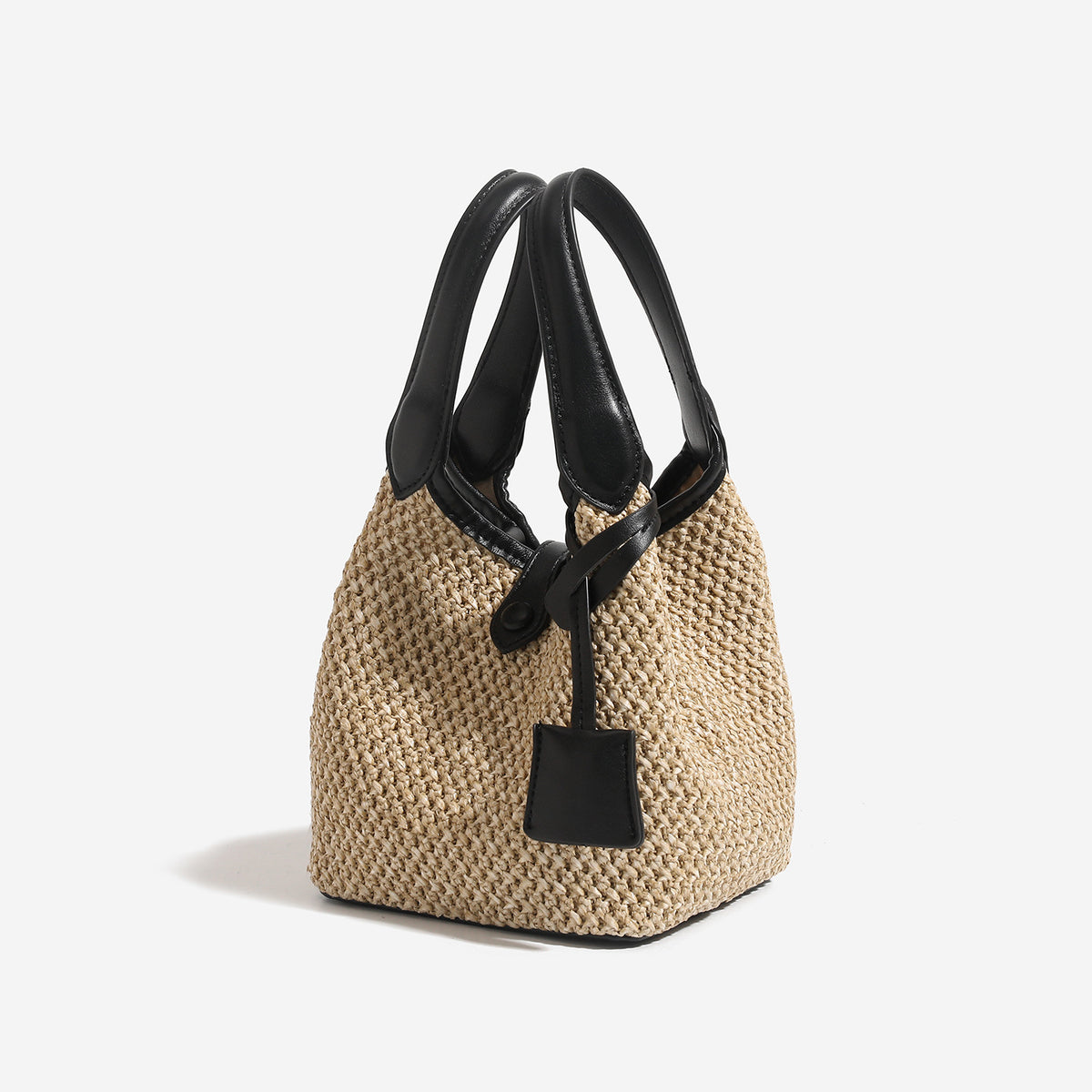 Woven beige straw bucket bag with black leather-look trim, dual top handles, detachable shoulder strap, and front snap