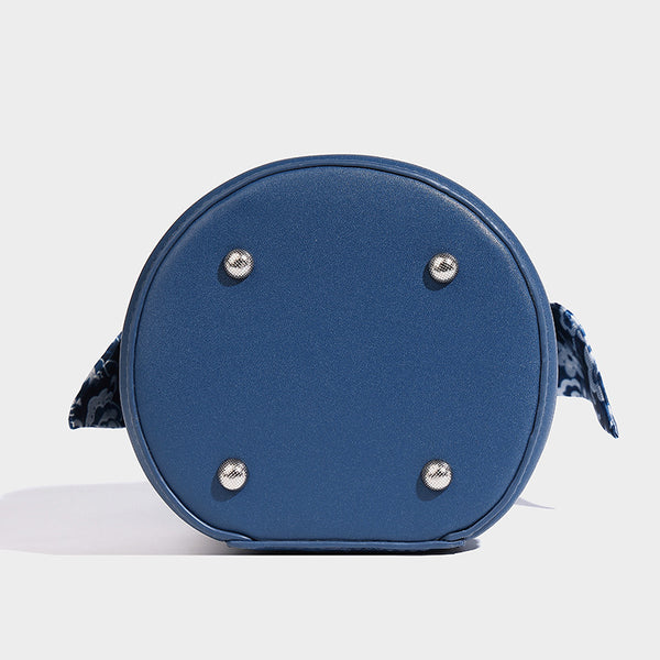Small cylindrical barrel bag in blue-and-white floral jacquard with leather-look trim, scarf-wrapped top handle, silver-tone