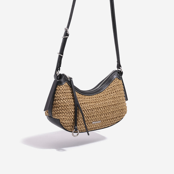 Tan woven straw half-moon shoulder bag with black leather-look trim, zip closure, tassel pull, and adjustable crossbody