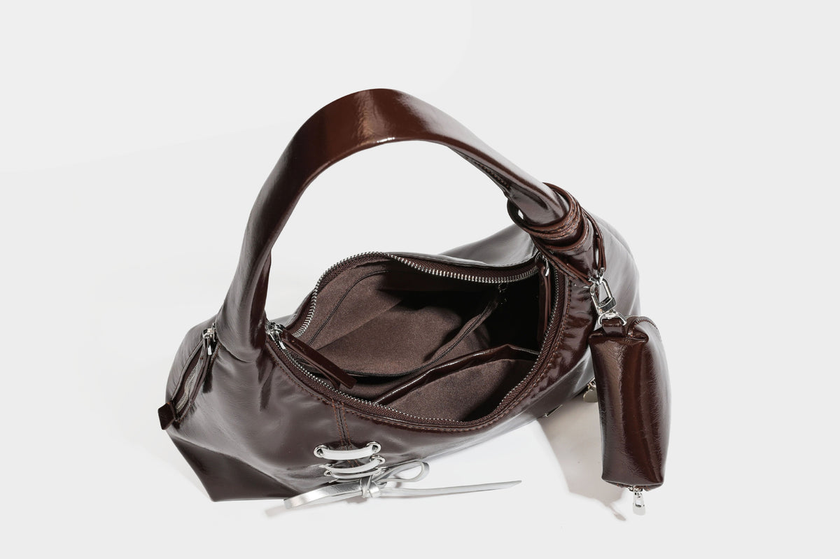 Weich fallende Hobo-Schultertasche in glänzender Lederoptik mit silberfarbenen Ösen zum Schnüren und Schleifenband auf der Vorderseite, Detailansicht