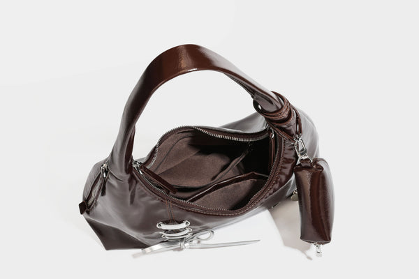 Weich fallende Hobo-Schultertasche in glänzender Lederoptik mit silberfarbenen Ösen zum Schnüren und Schleifenband auf der Vorderseite, Detailansicht