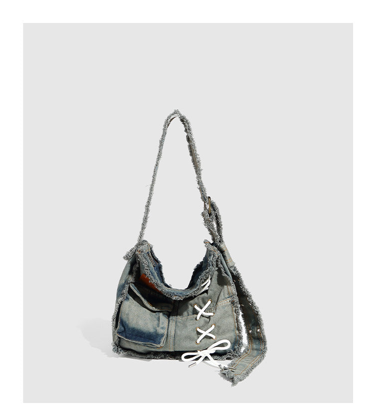 Slouchy distressed denim shoulder bag with frayed edges, white lace-up cross detail, front snap pocket, and long shoulder