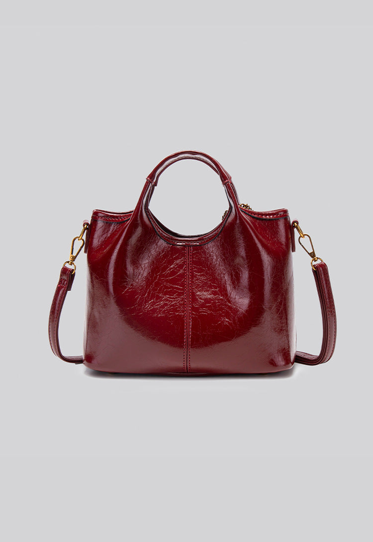 Structured crinkle-gloss top-handle satchel in deep burgundy with antique gold lock charm and detachable shoulder strap