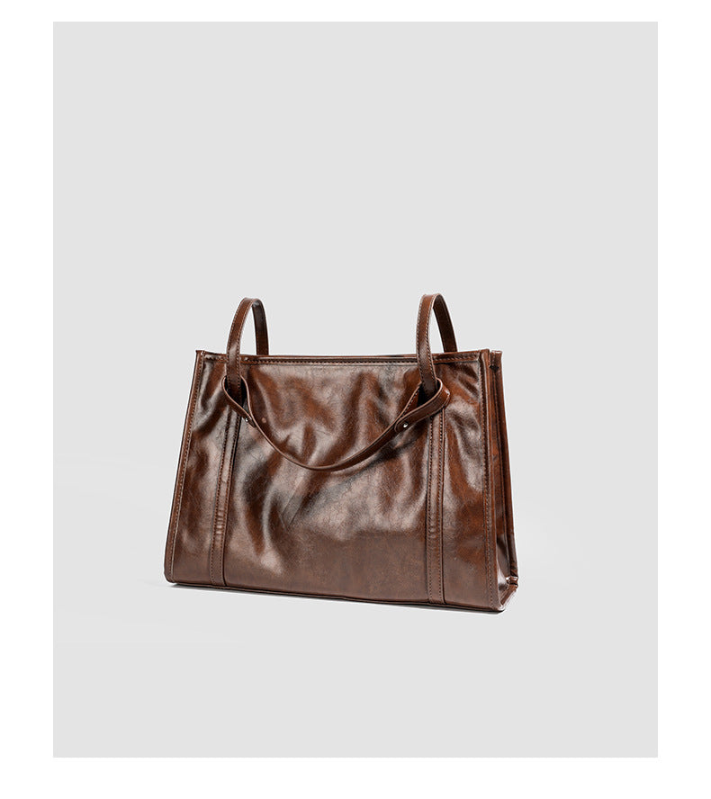Large structured glossy leather-look tote bag with dual top handles and long shoulder strap in burnished brown, detail view