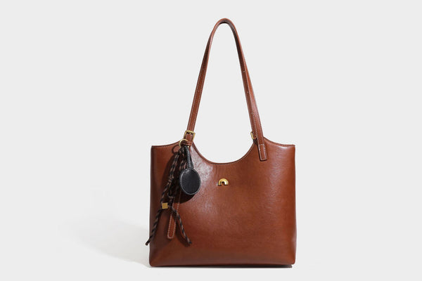 Structured smooth leather-look tote bag with long shoulder strap, gold-tone hardware, and hanging tassel-coin charm, detail