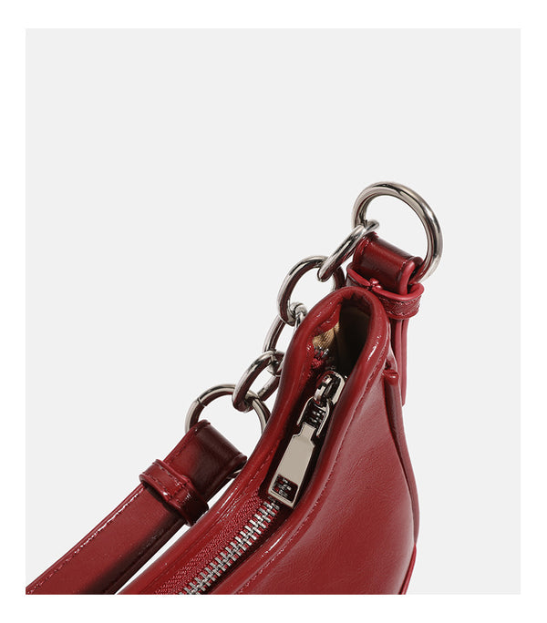 Small glossy cherry red crescent shoulder bag with silver chain strap, bead and tassel charm, and round pendant, detail view