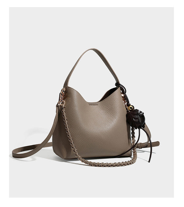 Hobo-Schultertasche in genarbtem Lederlook mit goldfarbener Kette als Schulterriemen, kurzem Tragegriff und dekorativem seitlichem Anhänger, Detailansicht