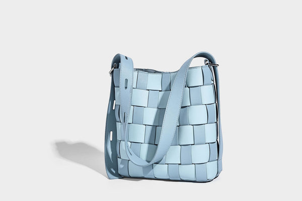 Hand-woven black-and-white checkerboard bucket bag with smooth black trim, silver-tone ring hardware, and adjustable