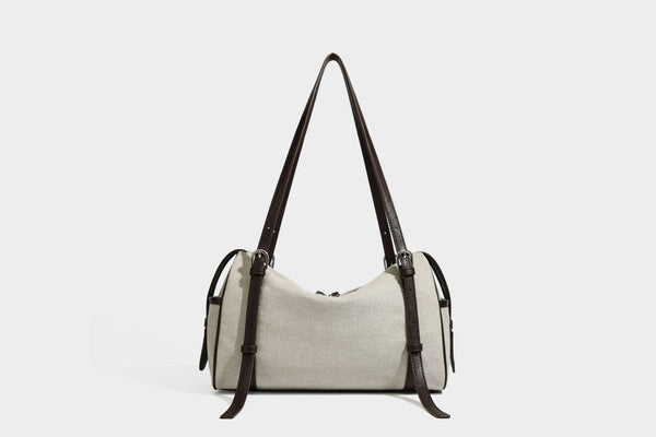 Beige canvas barrel bag with dark brown leather-look trim, silver-tone hardware, top zip closure, and adjustable shoulder