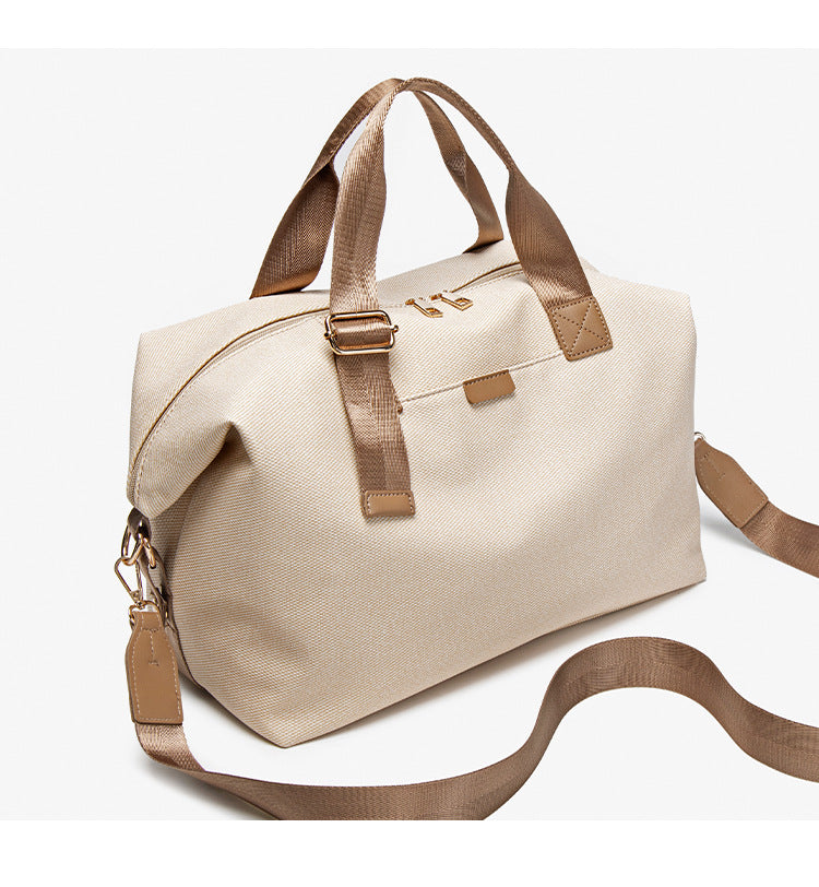 Structured woven duffel bag with dual tan webbing handles, detachable shoulder strap, top zip closure, and gold-tone