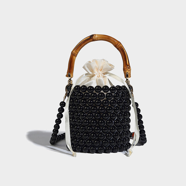 Small cylindrical bucket bag with glossy faux-pearl bead exterior, bamboo arched top handle, satin drawstring closure, and
