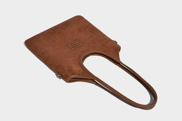 Tote-Bag in warmem Braun mit matter Wildlederoptik, langen Tragegriffen, geprägtem Logo, silberfarbenen Beschlägen und passendem, Detail