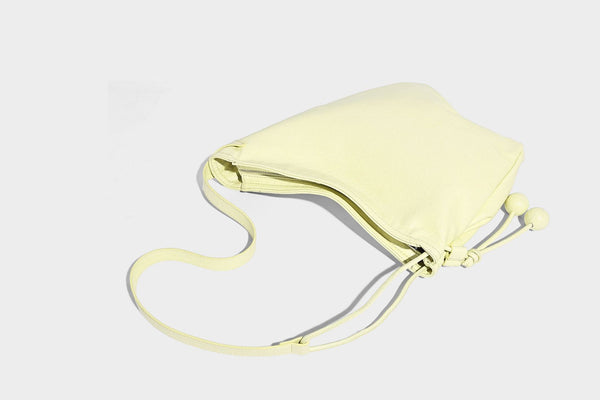 Slouchy hobo shoulder bag in pale yellow with slim strap, drawstring bead closure, and pink tulip floral charm, detail view