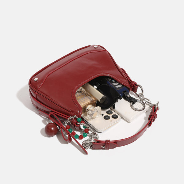 Small glossy cherry red crescent shoulder bag with silver chain strap, bead and tassel charm, and round pendant, detail view