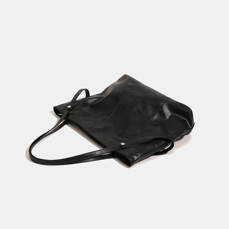 Große quadratische Shopper-Tasche in schwarzer Lederoptik mit zwei Schultergriffen und längerem Trageriemen, glatte glänzende Oberfläche und seitliche Beschläge