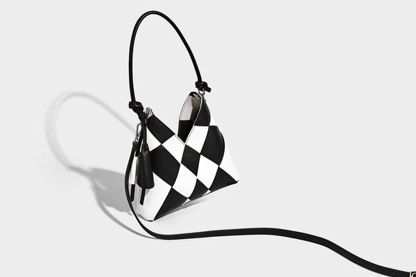 Compact bucket shoulder bag with black-and-white diamond patchwork panels, knotted top handle, gold-tone hardware, and