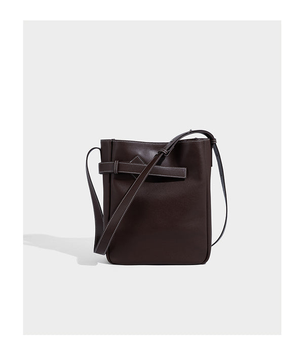 Structured dark brown leather-look bucket bag with white contrast stitching, front wraparound belt buckle strap, and long