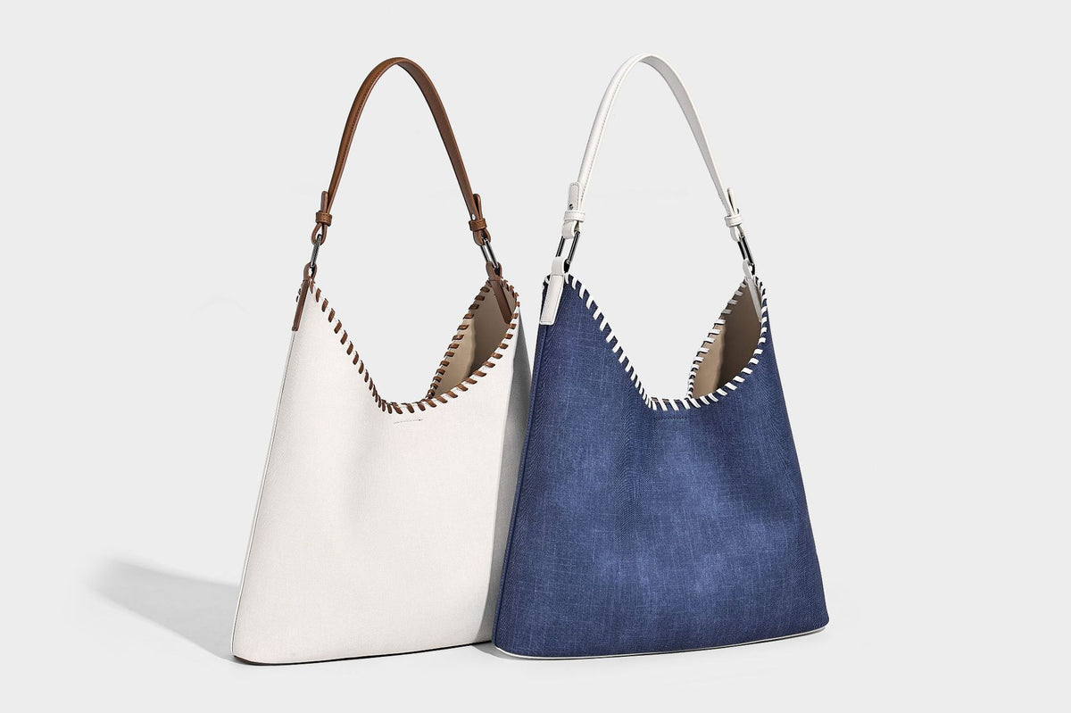 Denim-blue hobo tote with white leather-look shoulder strap, contrast whipstitch trim along curved open top, and silver-tone