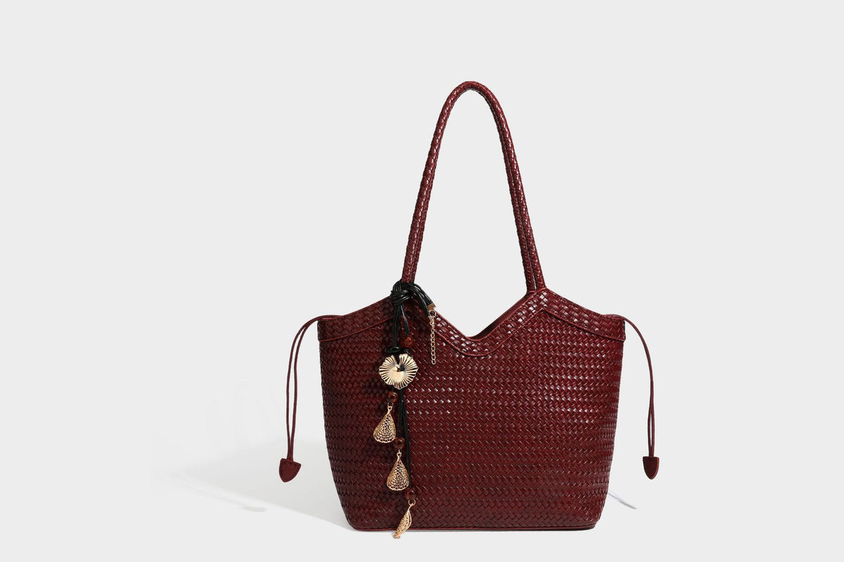 Olivgrüne Tote-Bag in Korbgeflecht-Optik mit dunkelbraunen geflochtenen Schulterriemen, seitlichen Kordelzügen und Perlenanhänger in Goldoptik