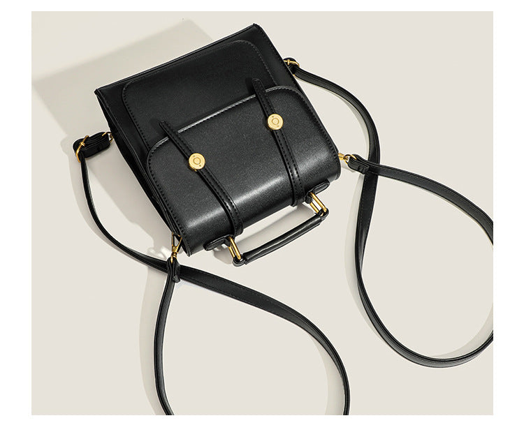 Structured mini satchel backpack with smooth leather-look finish, front flap pocket, gold-tone stud closures, and top handle