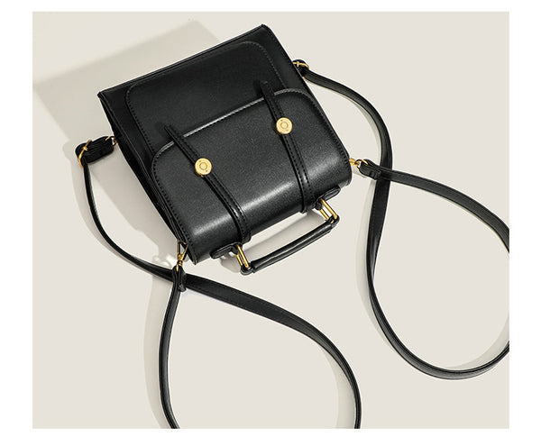 Structured mini satchel backpack with smooth leather-look finish, front flap pocket, gold-tone stud closures, and top handle