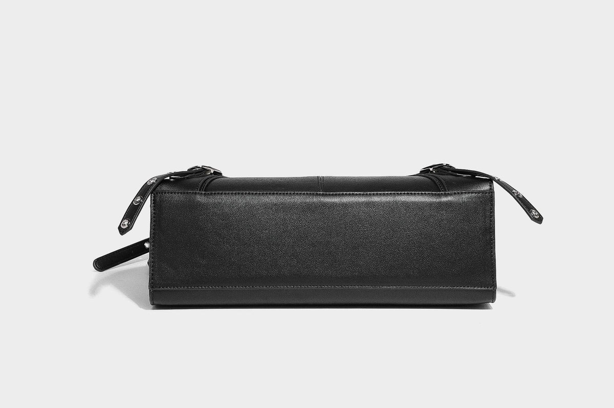 Black structured rectangular satchel bag with silver-tone rivets, large front buckle strap, zip pockets, dual top handles