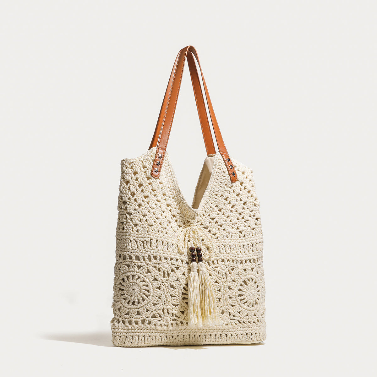 Cream openwork crochet tote bag with tan leather-look double shoulder straps and tassel drawstring tie, detail view 2