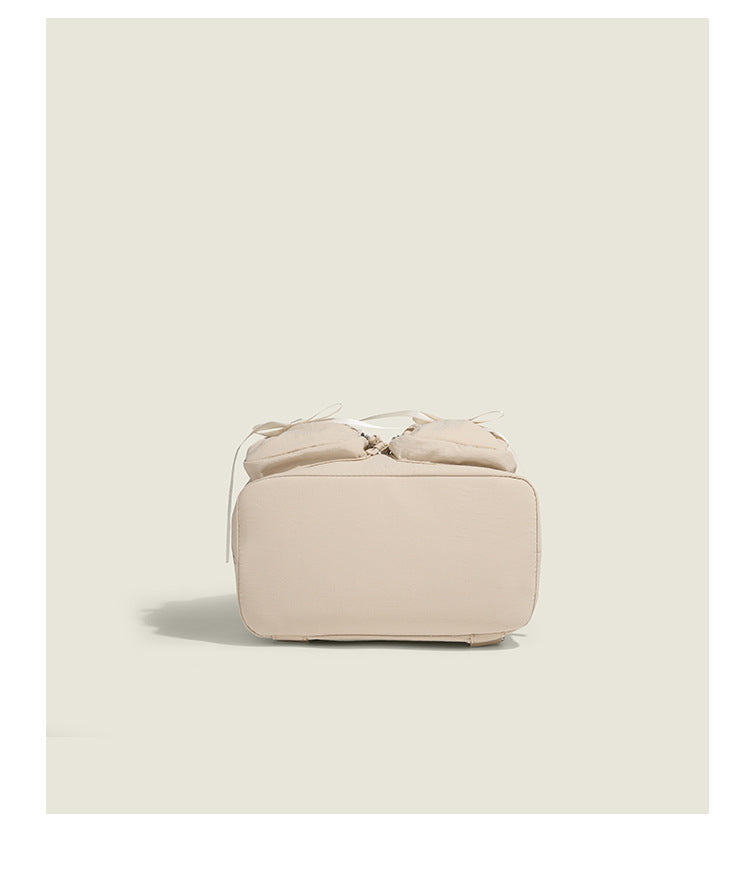 Soft matte nylon drawstring backpack with ruched bow-detail front zip pockets, top carry handle, and silver-tone hardware