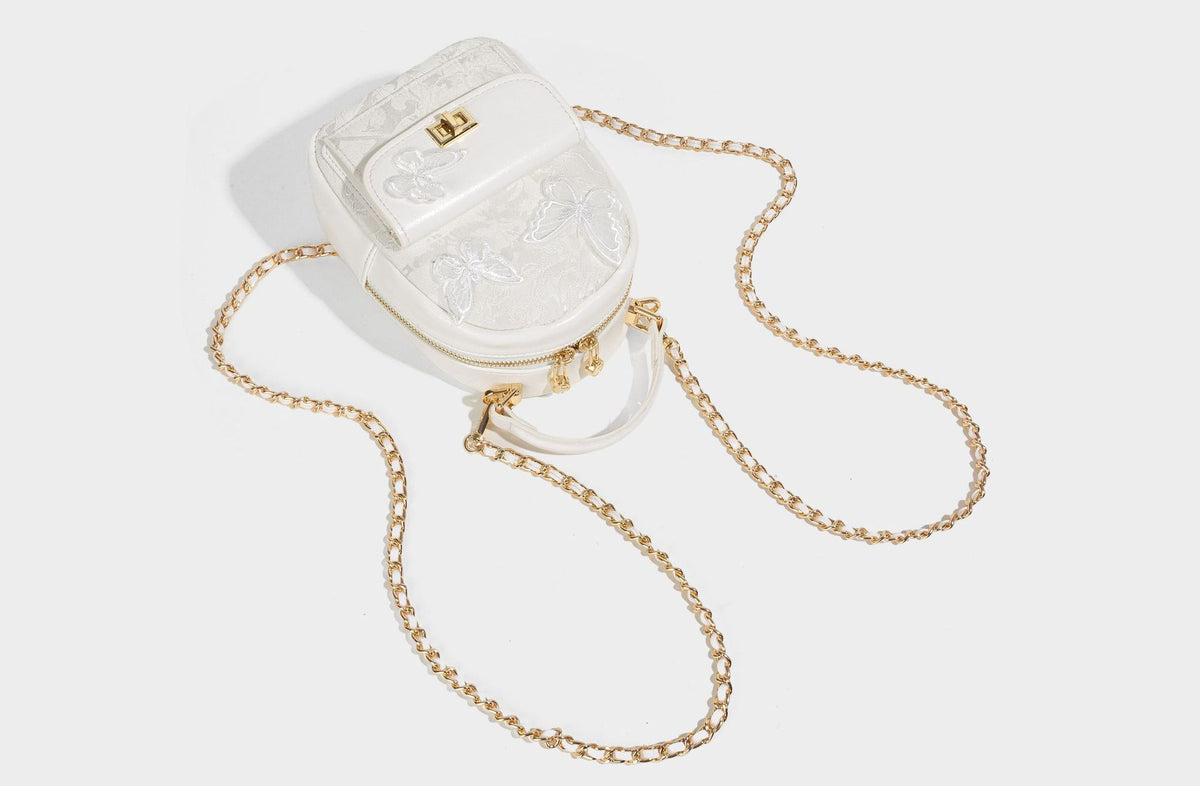 Structured mini backpack handbag with butterfly embroidery, gold-tone chain strap, and turn-lock front flap pocket, detail