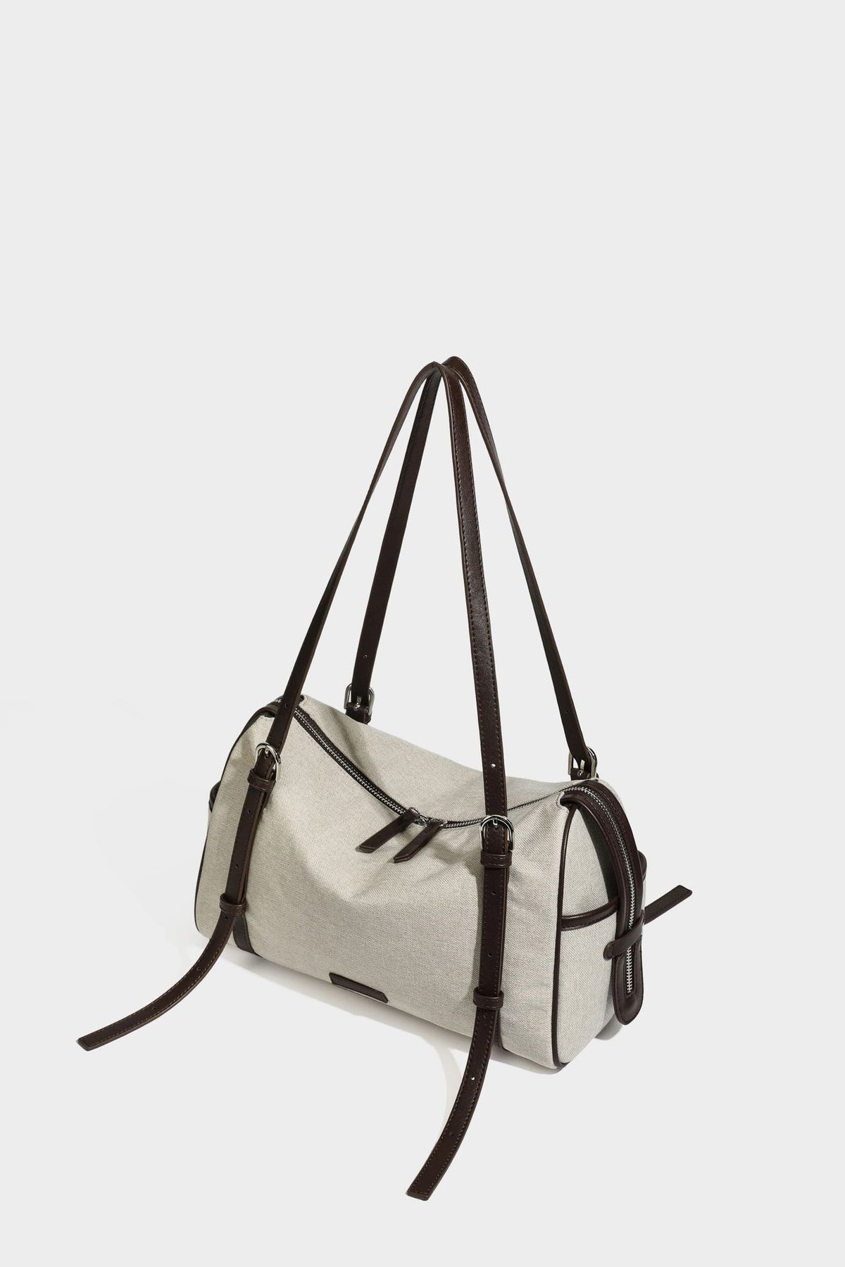 Beige canvas barrel bag with dark brown leather-look trim, silver-tone hardware, top zip closure, and adjustable shoulder
