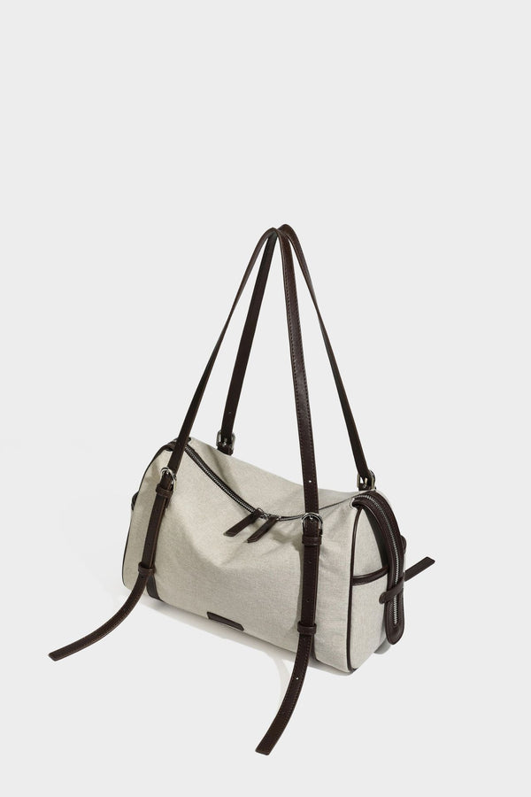 Beige canvas barrel bag with dark brown leather-look trim, silver-tone hardware, top zip closure, and adjustable shoulder