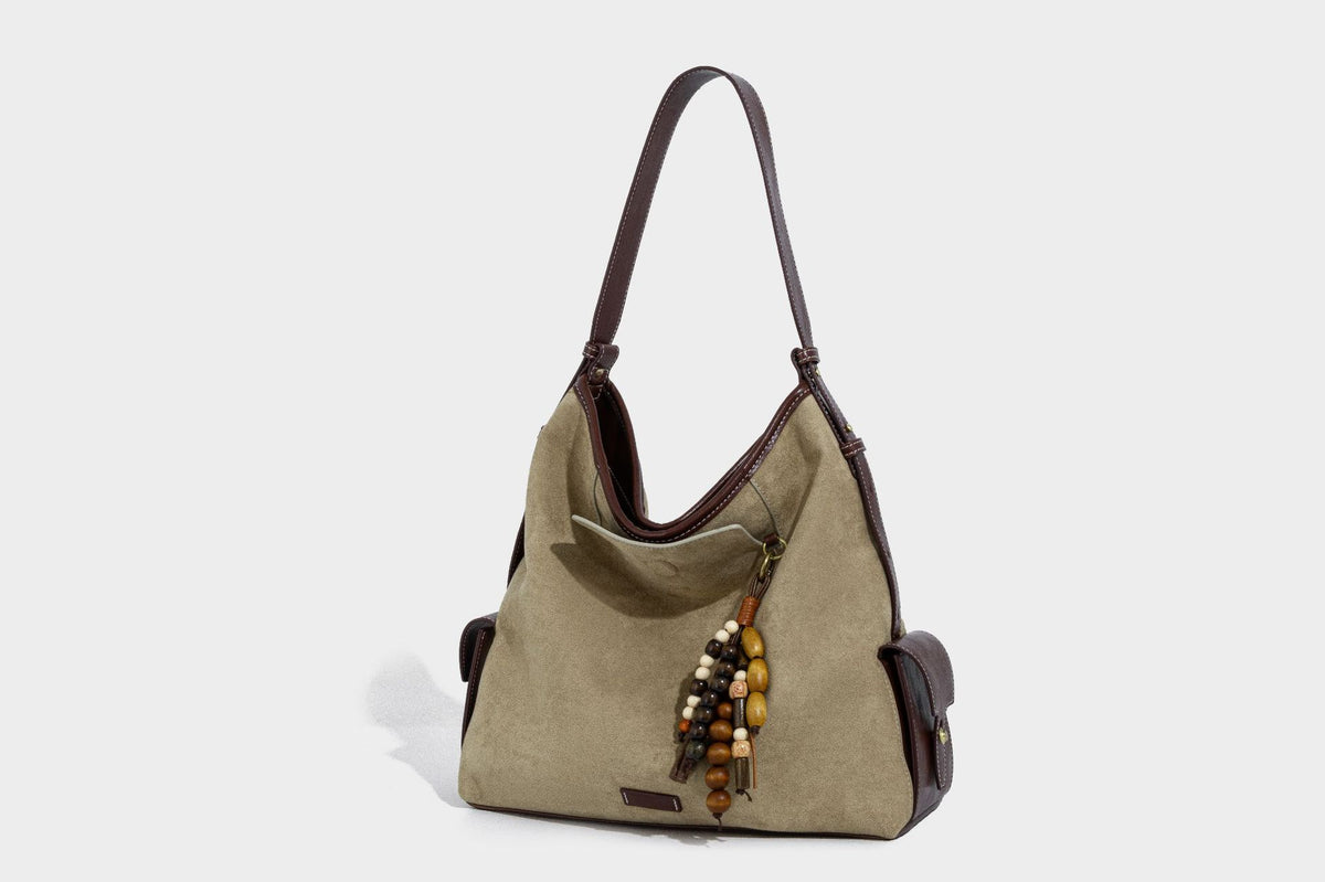 Lässig fallende Hobo-Schultertasche in Khaki aus mattem Material in Wildlederoptik mit dunkelbraunem Besatz in Lederoptik, Quastenanhänger mit Perlen und seitlicher Klappe, Detailansicht