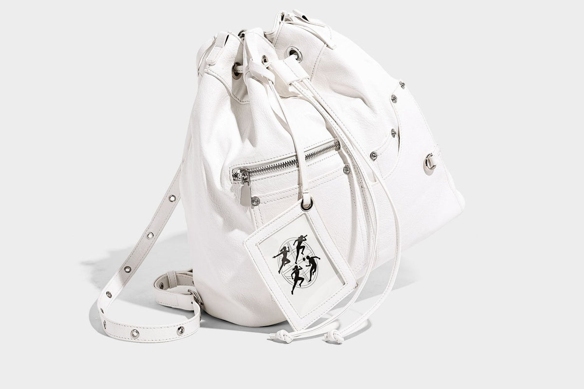 Glossy black convertible bucket backpack with silver grommet-studded straps, drawstring cinch closure, and front zip pocket