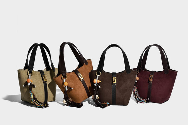 Small structured trapezoid tote bag in matte suede-look finish with black contrast trim, gold-tone front clasp, tassel charm