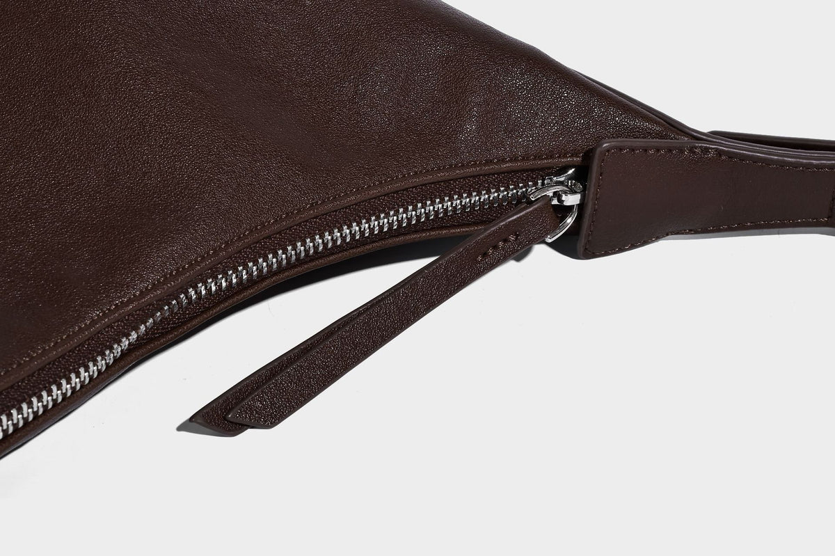 Slouchy bucket hobo shoulder bag in dark brown with glossy leather-look finish, top zip closure, and long adjustable, detail