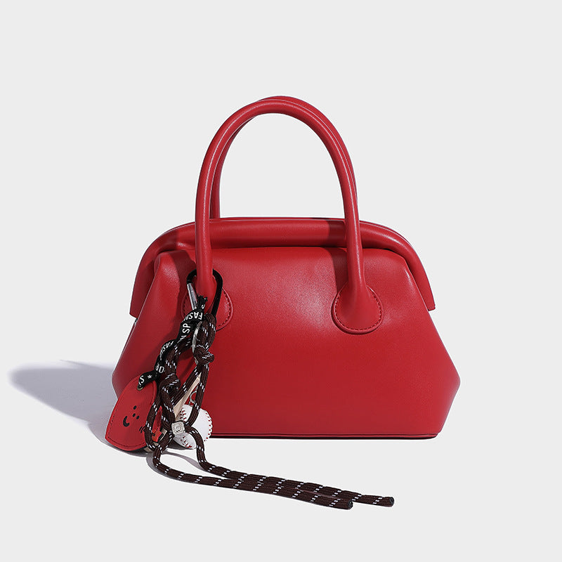 Small structured shell top-handle bag in red with heart charm and braided cord detail, smooth leather-look finish, detail