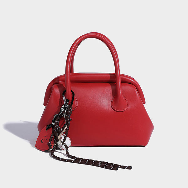 Small structured shell top-handle bag in red with heart charm and braided cord detail, smooth leather-look finish, detail