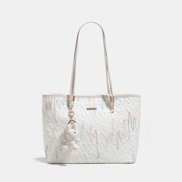 Off-white structured tote bag with dual shoulder straps, gold-tone hardware, and plush bear charm, front view