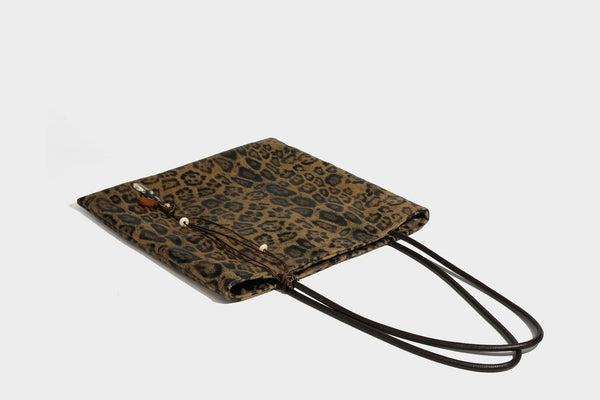 Large leopard print shoulder tote bag in tan and brown with slim dark straps and dangling beaded charm hardware, detail view